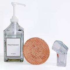 Mouthwash bottle with pump, woven coaster, and small glass container on a white background